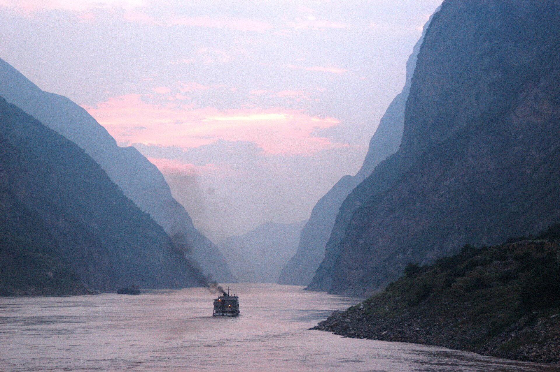 A passenger boat moving through the Yangtze River at dusk